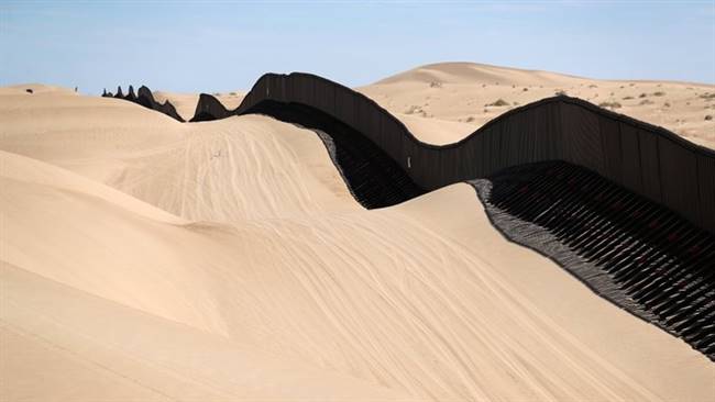 Một phần hàng rào biên giới chạy qua sa mạc ngăn cách giữa bang Arizona của Mỹ và bang Sonora của Mexico. Với chiều cao khoảng 4,5 m, các bộ phận của bức tường có thể nâng lên bằng máy và đặt trở lại vị trí ban đầu nhằm đối phó với những cơn bão cát có thể chôn vùi chúng. Ảnh: CNN.