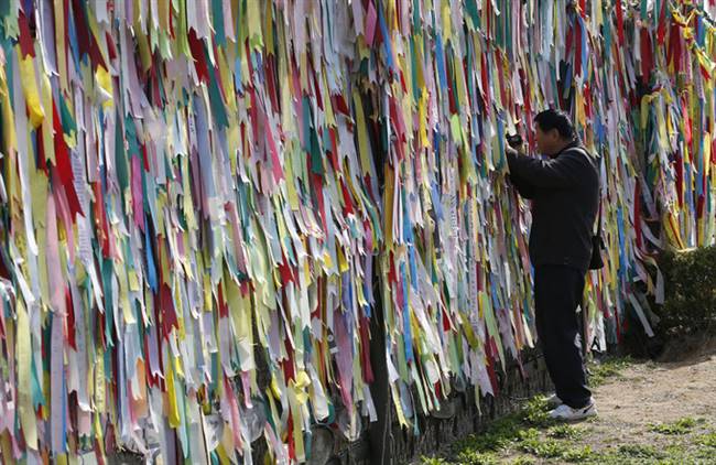 Một du khách quay phim qua khe hở của hàng rào biên giới ngăn cách lãnh thổ Triều Tiên và Hàn Quốc. Trên hàng rào gắn các dải ruy băng của khách du lịch và người dân để lại với hy vọng về ngày tái thống nhất hai miền Triều Tiên. Ảnh: Lee Jin-man/AP.