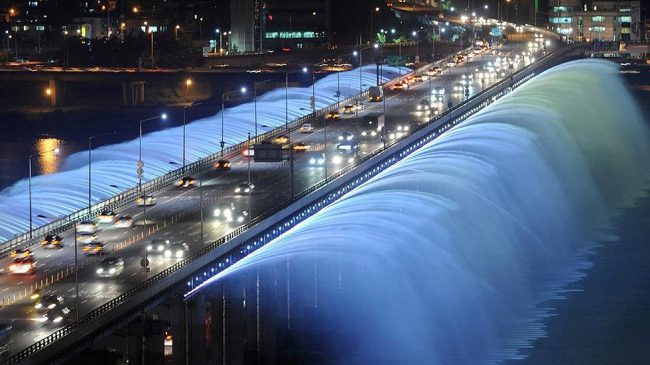 Thiết kế cầu khá công phu với 38 máy bơm công suất lớn, hút nước ở độ sâu 20 m, 380 vòi phun gắn bên thành cầu, đạt công suất bơm được 190 tấn nước/phút, tạo ra những dải nước dài 43 m hắt vổng theo chiều ngang, rồi dội xuống sông Hàn. Cây cầu còn trang bị hệ thống ánh sáng rất tỉ mỉ với 10.000 đèn LED treo hai bên thành cầu dài tới 1.140 m, tạo ra 200 mảng màu sắc khác nhau. Bởi vậy, chiếc cầu này còn được người dân xứ sở kim chi gọi bằng cái tên “cầu vồng ánh trăng”. Ảnh: KoreaToDo