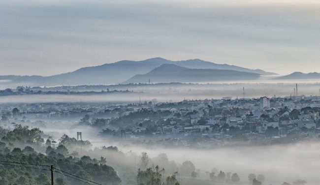 Một góc thành phố Pleiku đoạn cầu Phan Đình Phùng trong sương mù buổi sáng tháng 6. Anh Hoàng Quốc Vĩnh, một tay máy, cho biết sương hòa quyện với mây từ ngọn Hàm Rồng cao trên 1.000 m tràn xuống thung lũng tạo nên "cảnh đẹp tựa chốn thần tiên".